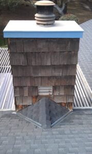 Chimney on shingled roof with blue trim.