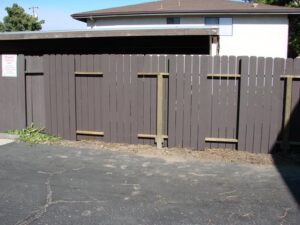 Brown wooden fence with missing boards near driveway.