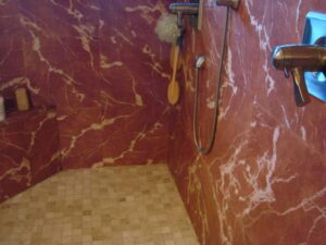 Bathroom with red marble walls and shower system.