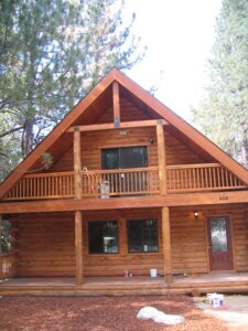 Rustic log cabin with balcony amidst pine trees.