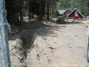 Construction site with trench near wooded area and houses.