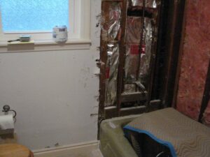 Bathroom under renovation with exposed insulation and pipes.