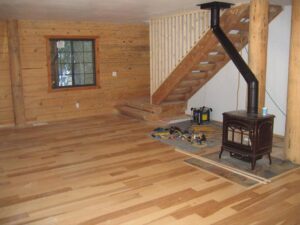 Wooden cabin interior with staircase and wood stove.