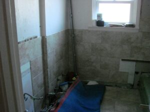 Unfinished bathroom renovation with exposed pipes and tiles.