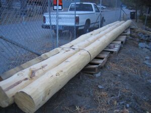 Utility poles stored beside chain-link fence and truck.