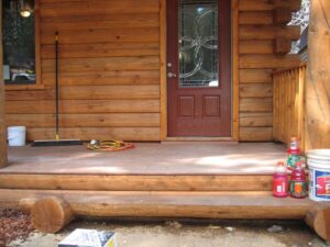 Wooden cabin porch with decorative door and supplies.